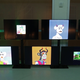 A wall of television screens displays several types of NFTs including bored apes.